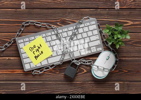 Sticky note with text BE RIGHT BACK, computer keyboard, chain and padlock on wooden background. Cyber security concept Stock Photo
