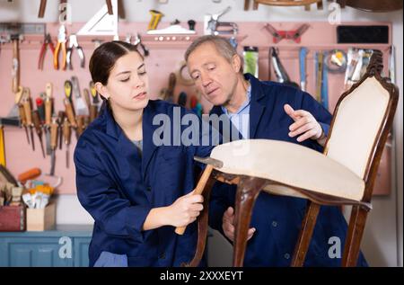 Senior male furniture maker and female apprentice working on vintage commode in workshop Stock Photo