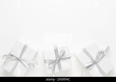 Three white gift boxes with silver ribbons on white background with copy space. Stock Photo