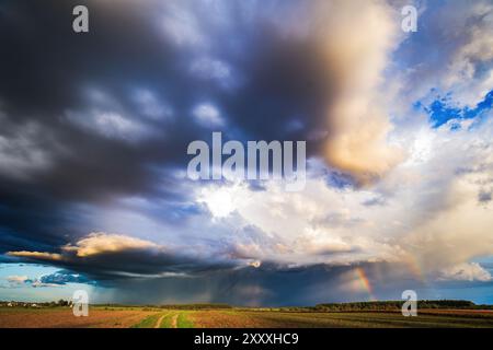 Storm clouds in the sky, rain on the horizon, summer season. Two rainbows Stock Photo