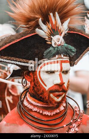 A man from Hela Province, Papua New Guinea, with vibrant face paint and a striking headdress adorned with feathers, symbolizing tribal pride. Stock Photo