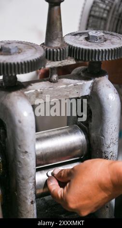 Goldsmith is using a rolling mill to shape metal for jewelry making Stock Photo