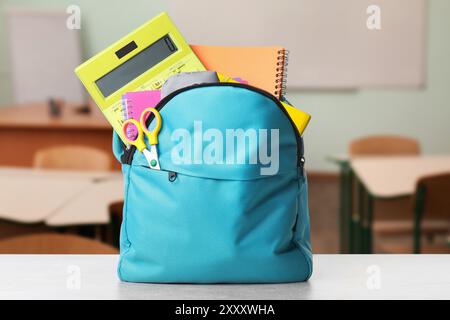 Light blue backpack with stationery on school desk in classroom Stock Photo