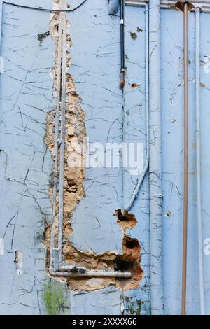 Old pipes exposed on broken wall with pealing blue paint Stock Photo