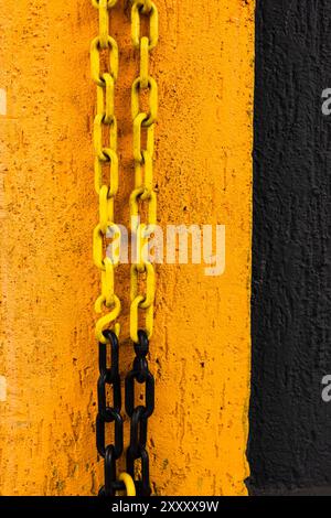 Yellow and black chain hanging from a yellow and black wall. Stock Photo
