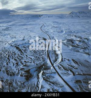 Aerial view of a long road winding through a vast snowy landscape with distant mountains under a cloudy sky, North, Iceland, Europe Stock Photo