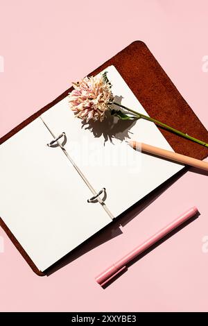 Open notebook beside pink pen and dried flower. Creativity and planning concept. Stock Photo