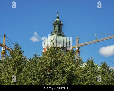 A church with a green dome behind trees and construction cranes on a clear sunny day, stockholm, baltic sea, sweden, scandinavia Stock Photo