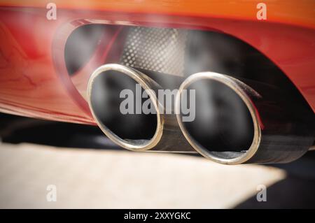 Close up of a red car dual exhaust pipe with smoke around it Stock Photo