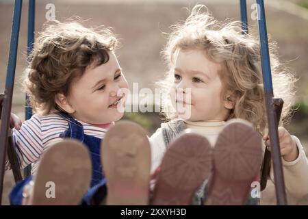 Twin baby sisters playing on swing in autumn park Stock Photo