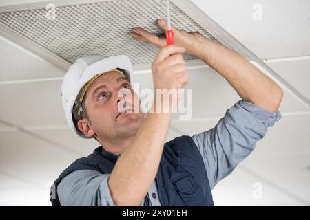 workman securing screws on ceiling vent Stock Photo