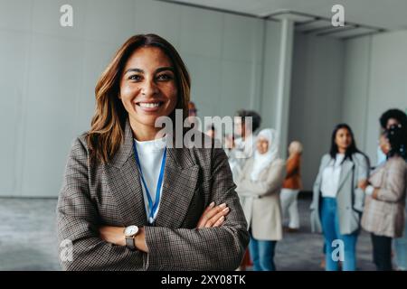 Happy businesswoman smiling at a conference with a diverse group of professionals in the background, showcasing leadership and inclusivity in a corpor Stock Photo