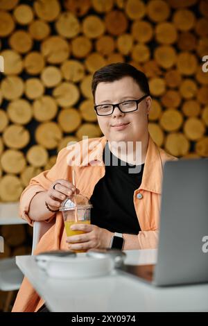 A man with Down syndrome works on his laptop in a cafe, enjoying a refreshing drink. Stock Photo