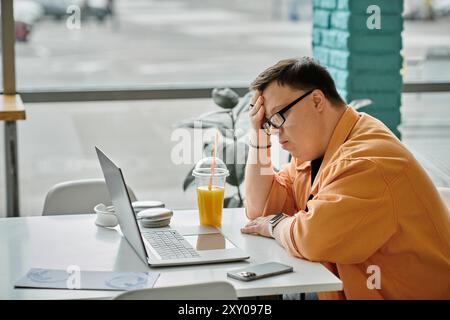 A man works remotely on his laptop in a cafe, enjoying a refreshing drink. Stock Photo