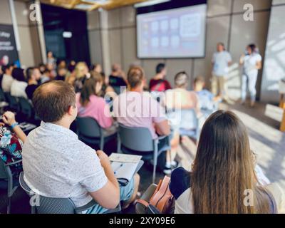 Group of individuals in a professional setting engage with presentation. Diverse audience focuses on speakers during conference session Stock Photo