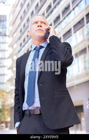 Smiling businessman having a telephone conversation on his smartphone outdoors. Stock Photo