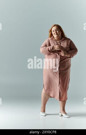 A woman in a long pink dress stands with her arms crossed, smiling in a studio. Stock Photo