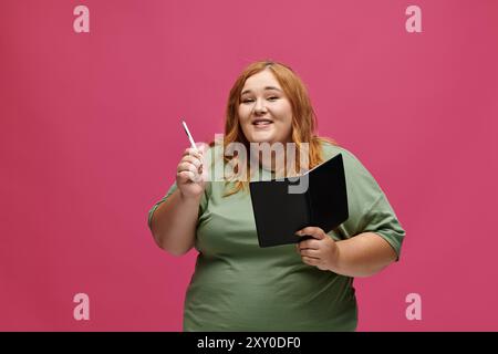 A woman smiles confidently while holding a pen and notebook. Stock Photo