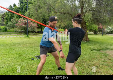 Two people engage in resistance band exercises outdoors, taking advantage of the park's green environment for their strength training session Stock Photo