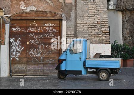Italy, Rome: blue Piaggio 125cc scooter in a city street, parked in front of an old brick house with its wooden door tagged Stock Photo