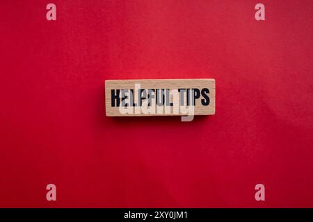 Helpful tips message written on wooden block with redbackground. Conceptual helpful tips symbol. Copy space. Stock Photo