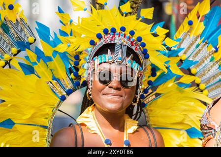 Black female wearing brightly coloured feather plumage at the Notting Hill Carnival Grand Parade 2024. Adult's Day on Bank Holiday Monday. Stock Photo