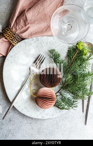 Top view of a stylish Christmas table setting featuring a marble plate, chic cutlery, a pink napkin, and decorative ornaments against a textured concr Stock Photo