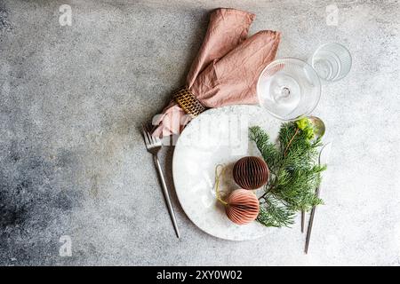 Top view of a stylish Christmas table setting featuring a marble plate, chic cutlery, a pink napkin, and decorative ornaments against a textured concr Stock Photo