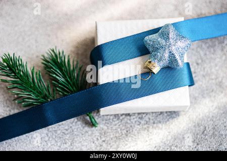 Elegant Christmas gift box wrapped with a blue ribbon and adorned with a glittering star ornament and pine needles against concrete texture background Stock Photo