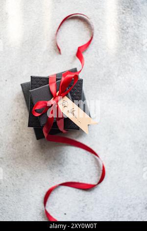 Top view of a stylish black gift box tied with a vibrant red ribbon and featuring a handwritten tag that reads For you..., placed on a textured gray b Stock Photo