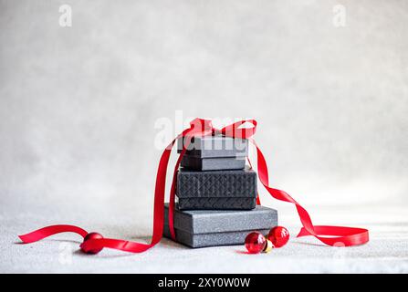 Top view of stacked Christmas gift boxes tied with a shimmering red ribbon, accompanied by red baubles on a textured gray backdrop. Stock Photo