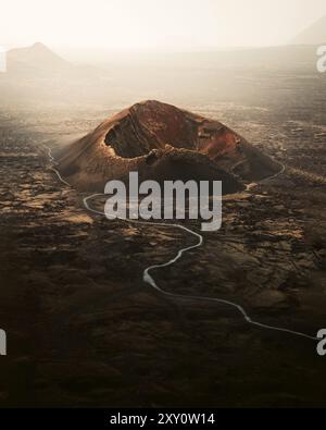 This stunning aerial image captures the Cuervo Volcano in Lanzarote, Canary Islands The volcanic landscape is highlighted by the crater and a winding Stock Photo