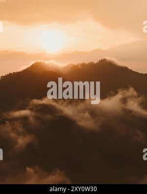 Captivating view of soft golden sunlight breaking through dense cloudy fog over the rugged peaks of the Himalayas during the enchanting golden hour. Stock Photo
