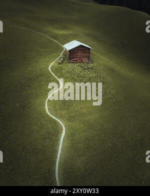 A cozy wooden cabin secluded in the Swiss Alps, accessible by a winding path through a lush green meadow. Stock Photo