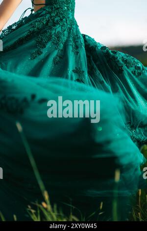 A close-up view of an elegant emerald green prom dress worn by a teenager, featuring intricate floral embroidery, set against a natural outdoor backdr Stock Photo