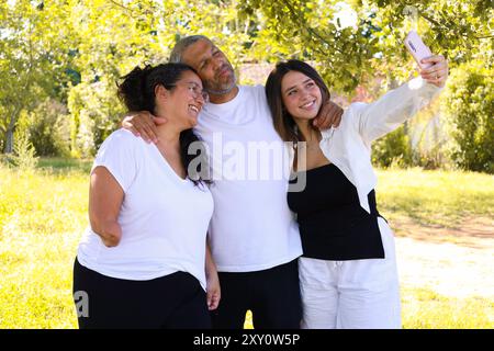 A family consisting of a man, a woman with an arm amputation, and a young woman, share a joyful moment together in a park, taking a selfie Stock Photo