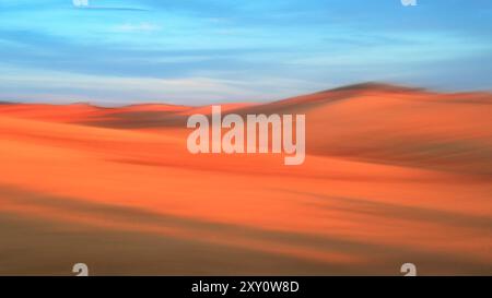A tranquil image capturing the flowing sand dunes of a desert at sunset The soft focus effect creates a surreal, dreamy atmosphere with rich orange an Stock Photo