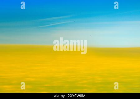 A vibrant abstract image of a yellow field blurred into soft motion, with a clear blue sky above The image captures the essence of a serene landscape, Stock Photo