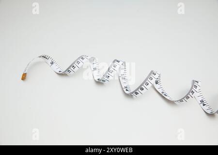 Top view of a simple white measuring tape loosely curled on a clean white background, emphasizing minimalism and precision in measurement tools. Stock Photo