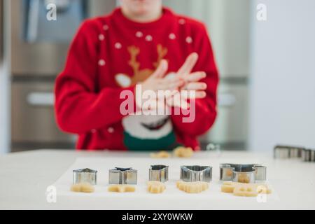 A child in a kitchen, wearing Christmas sweaters, engaging in cookie making The focus is on their hands and the various cookie cutters on the counter Stock Photo