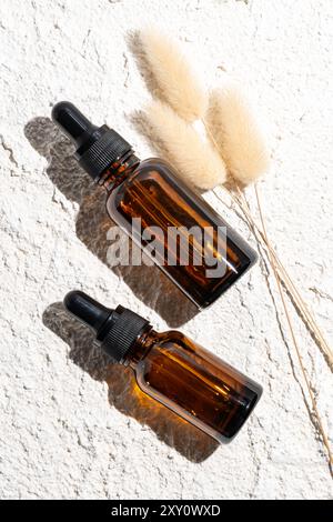 Image depicts two amber glass dropper bottles filled with essential oils, positioned artistically on a textured white stone background accompanied by Stock Photo