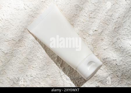 A neatly presented white cosmetic tube lies against a textured stone background, highlighting a clean and minimalist aesthetic ideal for health and be Stock Photo
