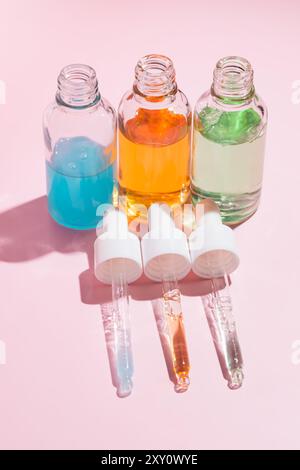 Three glass serum bottles with vibrant blue, amber, and green contents, accompanied by droppers against a pastel pink background, casting soft shadows Stock Photo