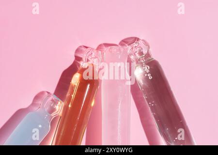 Top view of assorted skincare serum dropper bottles casting soft shadows on a pink surface, highlighting the beauty of cosmetic packaging. Stock Photo