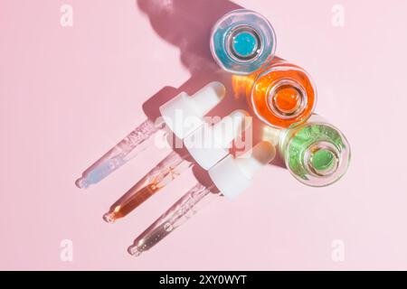 Top view of colorful serum dropper bottles arrayed on a soft pink background, casting subtle shadows. Stock Photo