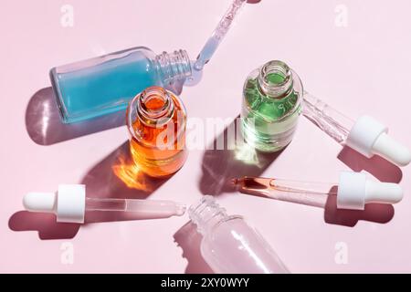 Top view of open serum dropper bottles with colorful liquids on a pink background, casting soft shadows in bright light. Stock Photo