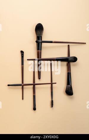 Top view of an assortment of professional makeup brushes arranged on a beige background, showcasing their different shapes and uses for cosmetic appli Stock Photo