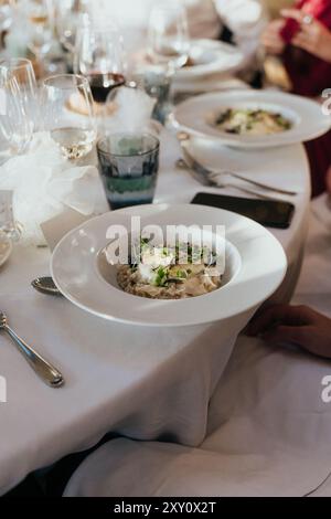 An elegant wedding dinner setting featuring a beautifully plated gourmet dish The image captures a white plate with a delicate pasta meal, surrounded Stock Photo