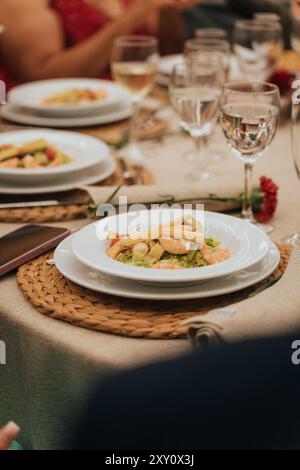 An elegant wedding reception dinner table featuring white plates with gourmet seafood salad, complemented by crisp wine glasses and tasteful decoratio Stock Photo