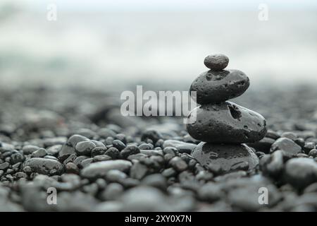 Three wet, black stones stacked in balance on a misty beach with smooth pebbles background. Stock Photo